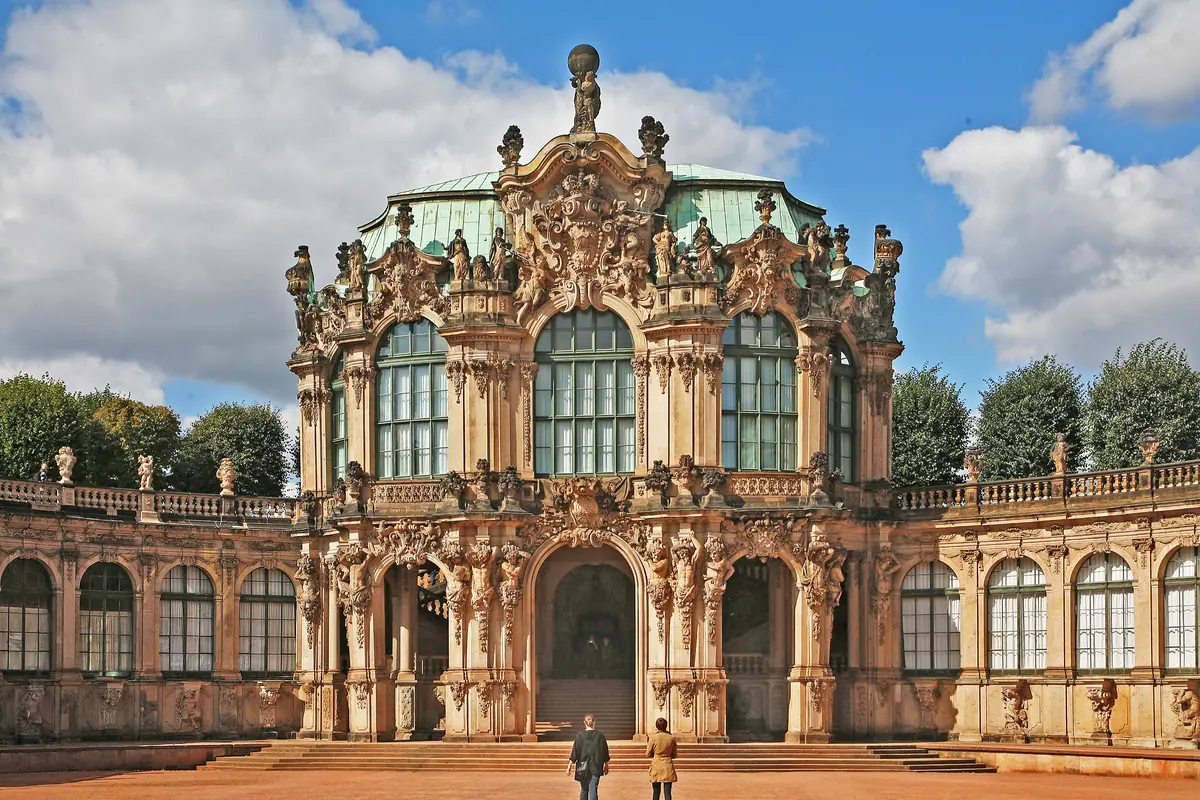 Forsiden af Wallpavillon i Dresden Zwinger med udskårne stenskulpturer, høje buevinduer, et grønt tag og to buede arkader på hver side.